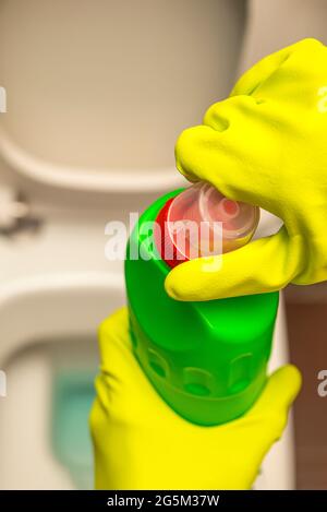 Pulizia e disinfezione dei servizi igienici. Aprire il detergente per wc prima dell'uso. Una mano con guanti pulisce il gabinetto con un disinfettante Foto Stock