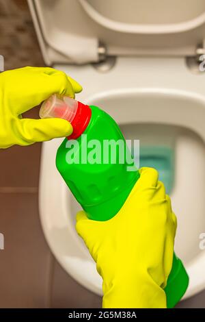 Pulizia e disinfezione dei servizi igienici. Aprire il detergente per wc prima dell'uso. Una mano con guanti pulisce il gabinetto con un disinfettante Foto Stock