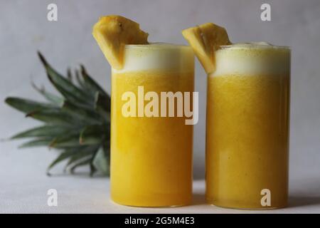 Succo di ananas freddo per battere il caldo estivo. Succo fatto in casa servito in lungo vetro decorato con un cuneo di ananas. Scatto su sfondo bianco Foto Stock