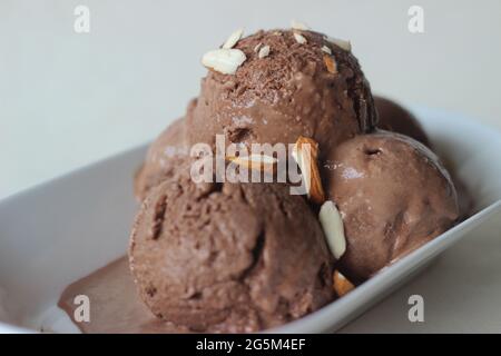 Scoop di gelato al cioccolato fatto in casa serviti con mandorle tritate. Scatto su sfondo bianco Foto Stock