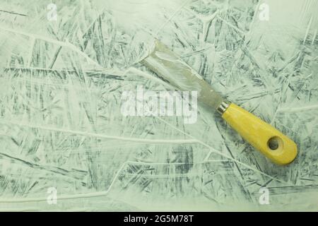 Cazzuola da costruzione sul tavolo durante il processo. Processo di ristrutturazione, sfondo con spazio per la copia. Coltello per stucco in un mastice sullo sfondo della parete Foto Stock