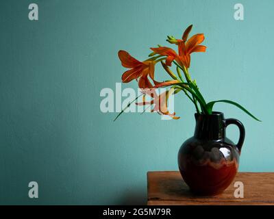 Giglio di tigre in vaso di ceramica con sfondo turchese ombra. Lilium lancifolium fiori arancioni bouquet su tavola in legno casa colonica. Estate cotagec Foto Stock
