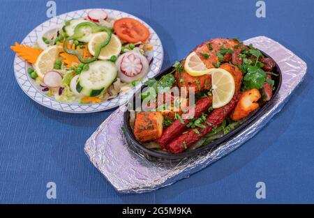 Carne alla griglia mescolata con salsa al pepe e verdure su fondo blu. Cucina indiana tradizionale. Foto Stock