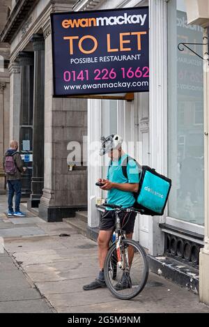 Lasciare segno e pilota Deliveroo controllare il suo telefono su Princes Street, Edimburgo, Scozia, Regno Unito. Foto Stock