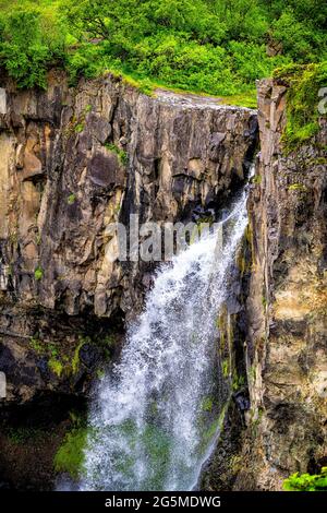 Hundafoss cascata alta angolo verticale closeup vista a Skaftafell, Islanda con acqua che cade dalla scogliera in verde estate lussureggiante in paesaggio roccioso Foto Stock