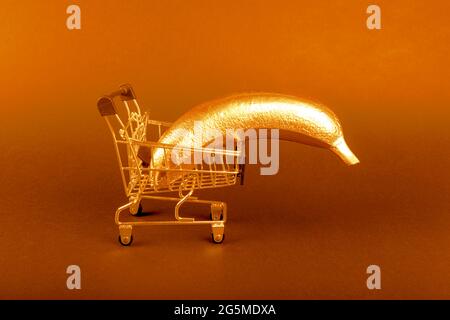 Banana d'oro in un carrello di shopping su sfondo arancione. Cibo creativo e concetto di frutta minimale. Concetto di vendita grande. Spazio di copia. Foto Stock