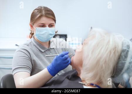 Dentista femminile che indossa una maschera medica per il viso, esaminando i denti del paziente anziano Foto Stock