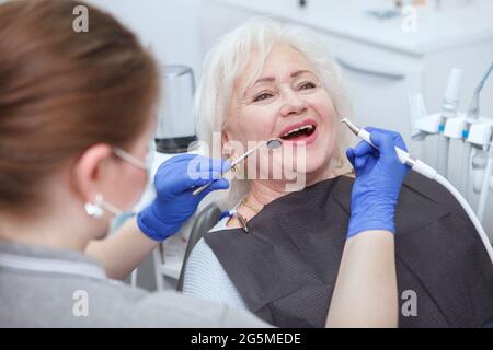 Donna anziana felice che ottiene il trattamento dentale dal dentista professionista Foto Stock
