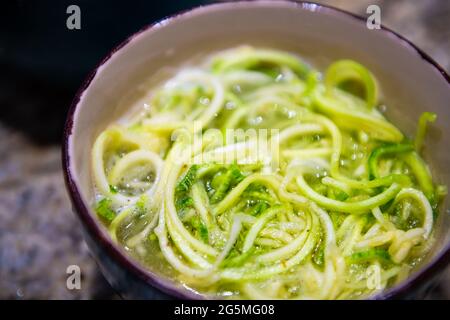 Closeup di zucchine grattugiate o di tagliatelle grezze di cetrioli pasta per preparazione di cottura vegana grezza o sostituzione di zuppa con acqua a basso contenuto di carb br Foto Stock