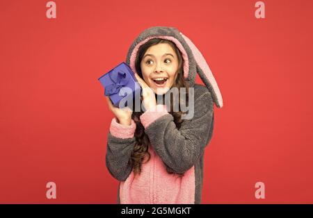 Bell'acquisto. Ragazza teen in pigiama conigliato. Bambino sorpreso indossare coniglio kigurumi e tenere scatola a sorpresa. Regali e regali. accessorio casa souvenir. Sentire Foto Stock