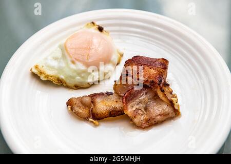 Macro closeup di fette di pancetta grassa cotta e uova fritte su piatto bianco a colazione brunch tradizionale americano pasto Foto Stock