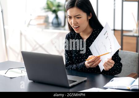 Infastidito dirigente di affari di donna asiatica arrabbiato, conduce una riunione con i colleghi in linea, parlando con una videochiamata, scolding per i risultati scarsi, mostrando il rapporto finanziario, umore negativo e irritato Foto Stock