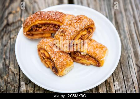 Closeup di pasta di rugelach confettura di noci su piatto bianco e tavolo di legno con cristalli di zucchero su involtini Foto Stock