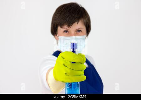 Il concetto di disinfezione e pulizia indoor.Cleaning signora spray da spray. Donna in uniforme e guanti di gomma che tengono detergente spray con pulito Foto Stock