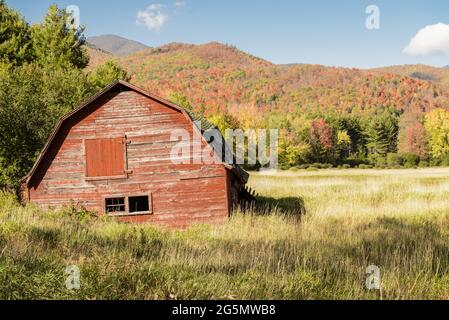 Antico, rustico, fienile rosso con alberi colorati sullo sfondo montuoso degli Adirondack Foto Stock