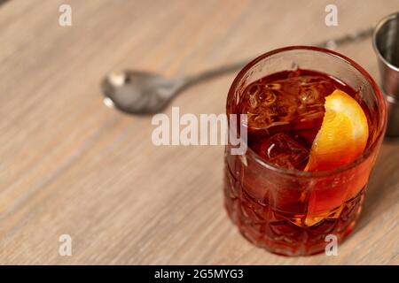 Vista panoramica del cocktail negroni con zeppa arancione su superficie in legno con cucchiaio di miscelazione Foto Stock