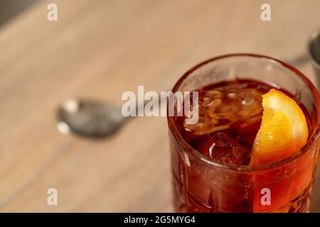 Vista ravvicinata del cocktail negroni con zeppa arancione su superficie in legno con cucchiaio di miscelazione Foto Stock