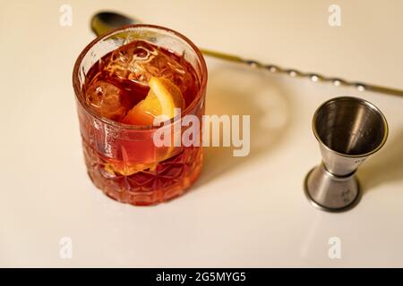 Vista panoramica del cocktail negroni con zeppa arancione su superficie bianca con cucchiaio e jigger Foto Stock