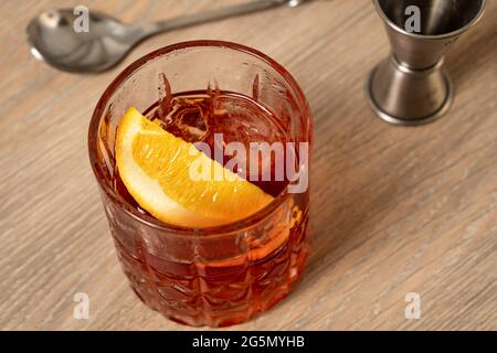 Vista ravvicinata del cocktail negroni su superficie in legno con cucchiaio e jigger sullo sfondo Foto Stock