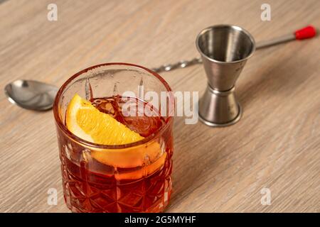Vista ravvicinata del cocktail negroni su superficie in legno con cucchiaio e jigger sullo sfondo Foto Stock