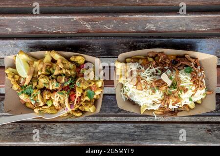 Vista dall'alto di porzioni da portare via di poutine alla moda, patatine fritte sulla parte superiore con pollo piccante, formaggio e maiale tirato, su panca di legno all'aperto. Foto Stock