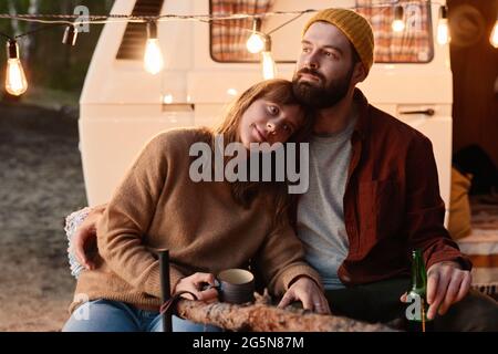 Romantica giovane coppia seduta vicino al fuoco e bere tè durante il picnic nella foresta Foto Stock