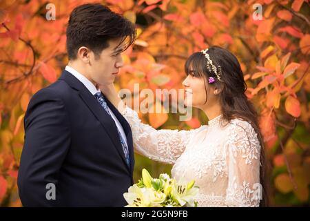 Sposa biraciale e sposo insieme all'aperto dopo il matrimonio autunnale con brillanti foglie arancioni colorate sullo sfondo Foto Stock