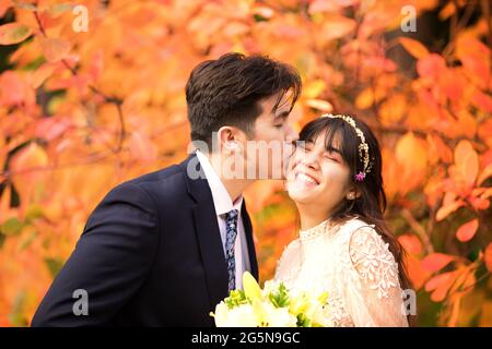 Biracial sposata coppia appena sposata baciando all'aperto da brillanti foglie arancioni d'autunno Foto Stock