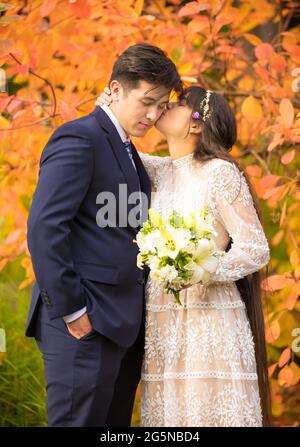 Biracial sposata coppia appena sposata baciando all'aperto da brillanti foglie arancioni d'autunno Foto Stock