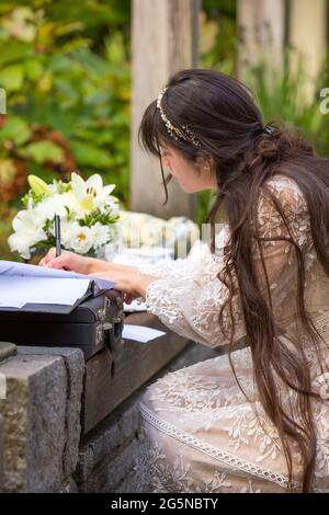 Nuova sposa biraciale che si inginocchiò fino a firmare il certificato di matrimonio dopo il matrimonio all'aperto Foto Stock
