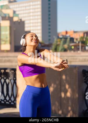 Foto verticale di una donna che allunga il corpo - riscaldamento prima di correre o allenarsi. Bracci di allungamento dei canali femmina prima di correre al mattino. Fitness Foto Stock