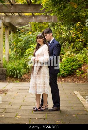Sposa biraciale e sposo all'aperto in posa sotto pergola ricoperta di vite Foto Stock