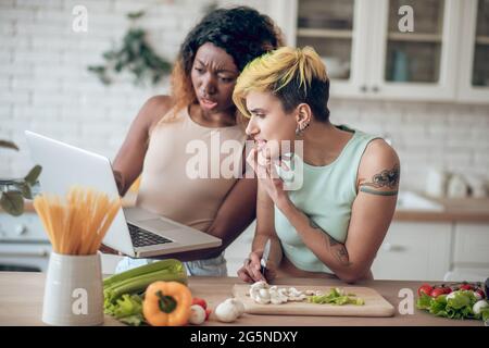 Le amiche che si interrogano emotivamente guardano indignate al notebook Foto Stock