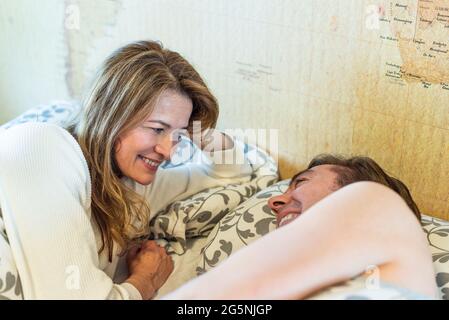 Coppia di mezza età che ride sdraiata sul letto. Foto Stock