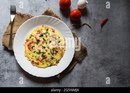 Frittata di pomodoro al formaggio o frittata spagnola a base di uovo con ingredienti aggiuntivi di formaggio, pepe, cipolla, aglio e pomodoro. Foto Stock