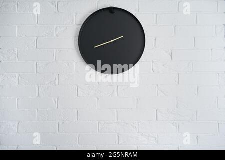 Orologio nero minimalista su una parete di mattoni bianchi all'interno Foto Stock