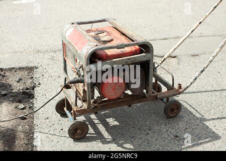 Generatore di benzina di elettricità. Alimentazione all'utensile elettrico. Generatore sulla strada per la riparazione stradale. Foto Stock