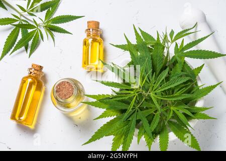 Olio di cannabis in bottiglie di vetro e foglie di cannabis a tavola bianca. Foto Stock