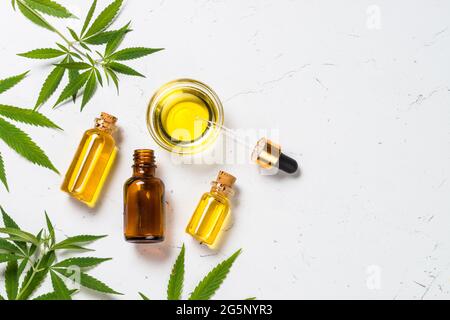 Olio di cannabis in bottiglie di vetro e foglie di cannabis a tavola bianca. Foto Stock