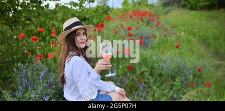 Giovane donna con vino Rosa in vetro su campo di papavero Foto Stock