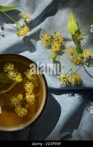 Tazza con tè tiglio, fiori e luce naturale Foto Stock