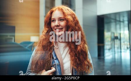 Studentessa vestita casualmente nel campus universitario. Giovane donna nel campus universitario con capelli rossi tinti. Foto Stock
