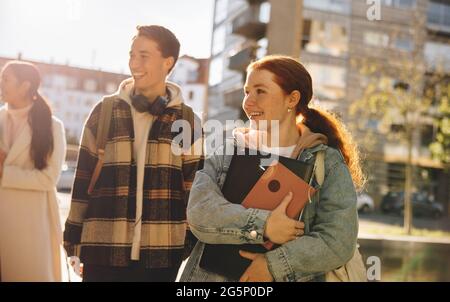 Amici che si guardano fuori mentre camminano con gli amici all'università. Studenti allegri che camminano all'aperto all'università. Foto Stock