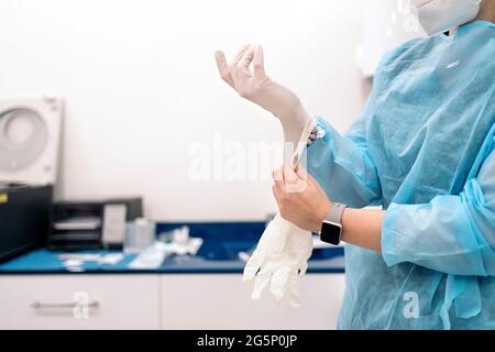 Operatore medico che indossa maschera facciale e indumenti protettivi che indossano guanti in lattice. Foto Stock