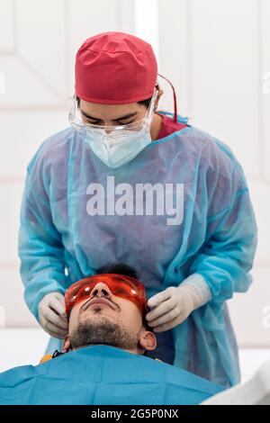 Uomo sdraiato in sedia dentale e indossando occhiali protettivi pronti all'uso macchina sbiancante. Foto Stock