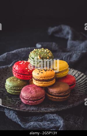 Macaron francesi colorati su un piatto nero, verticale con spazio per la copia Foto Stock