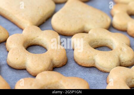 Biscotti shortbread cotti al forno sotto forma di fiori e cuori su una teglia da forno con carta pergamena appena tolta dal forno. Spuntino a base di tè per colazione. Foto Stock