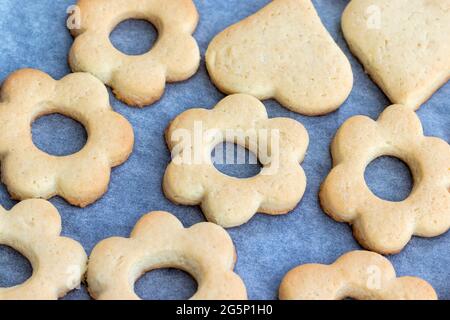 Biscotti shortbread cotti al forno sotto forma di fiori e cuori su una teglia da forno con carta pergamena appena tolta dal forno. Spuntino a base di tè per colazione. Foto Stock