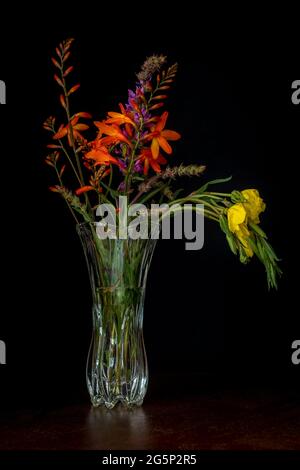 Vaso in vetro con sfondo nero di riferimento per fiori gialli e arancioni Foto Stock