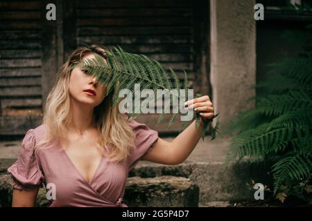 la giovane donna sta tenendo la foglia di felce tra le mani, coprendo parte del viso con essa. Il concetto di cosmetici naturali, la vita in campagna Foto Stock